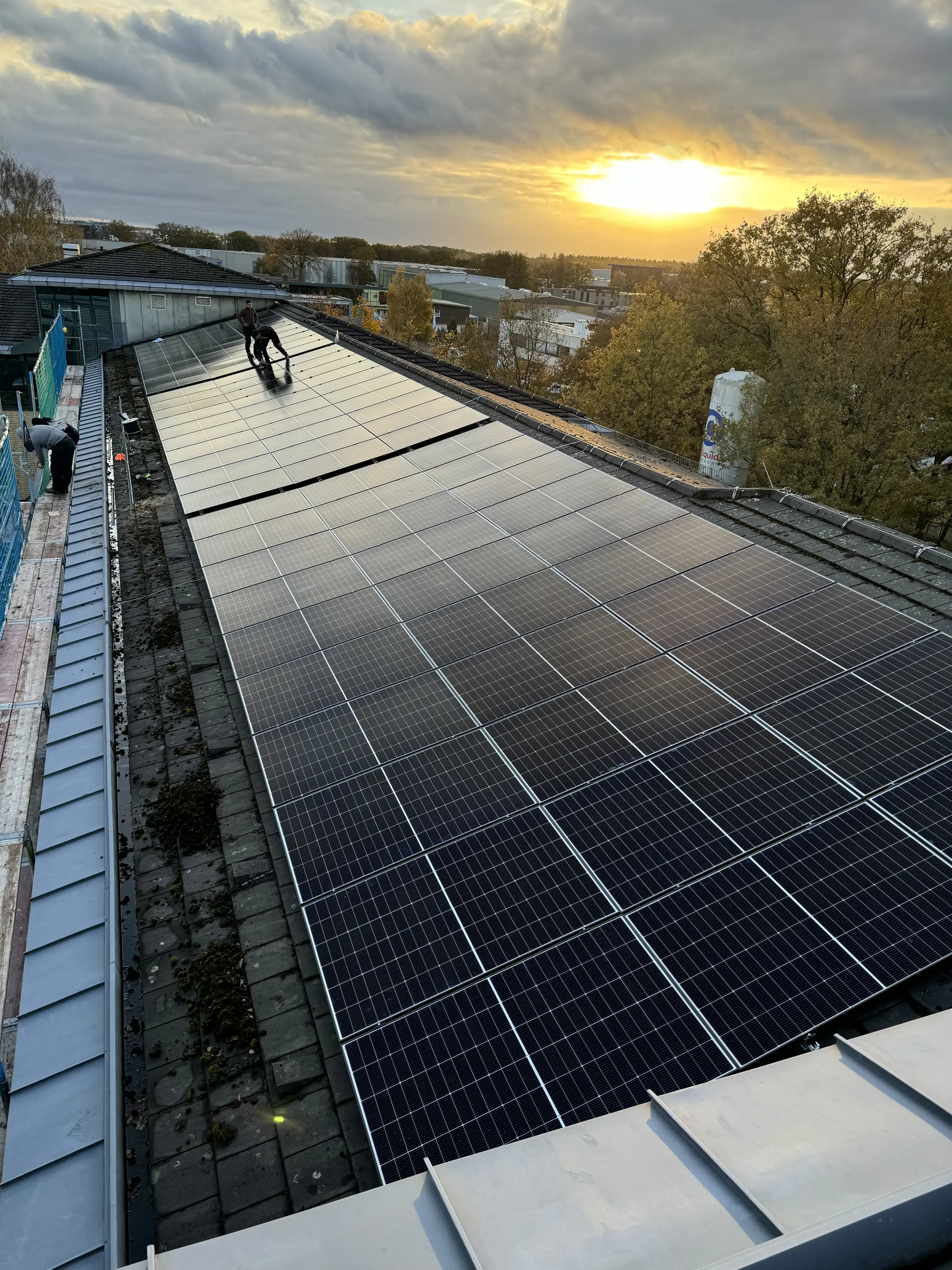 Photovoltaikanlage auf Gewerbedach wird bei Sonnenuntergang von Monteuren installiert und gereinigt.