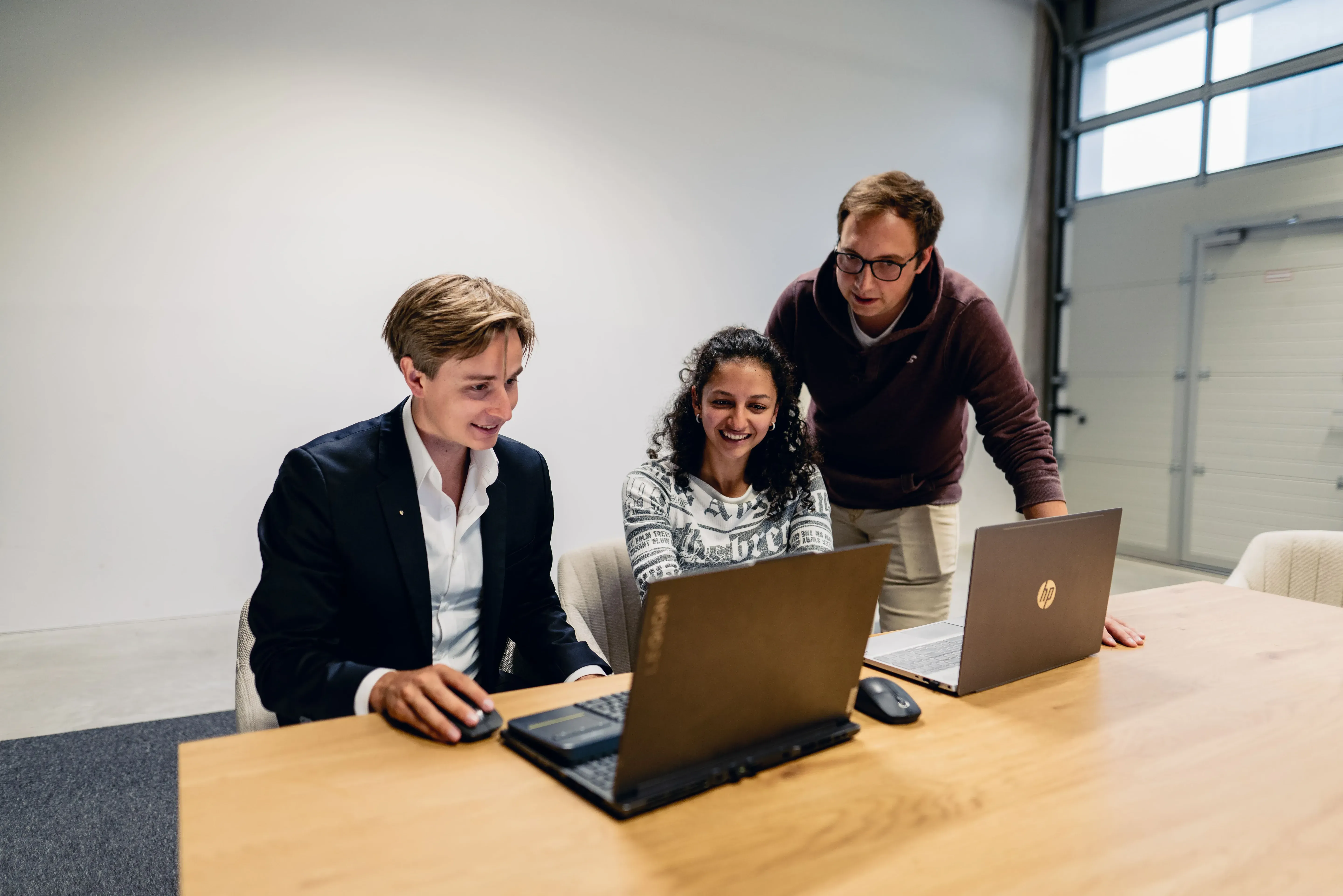 Drei junge Menschen arbeiten gemeinsam an Laptops in einem hellen Büro